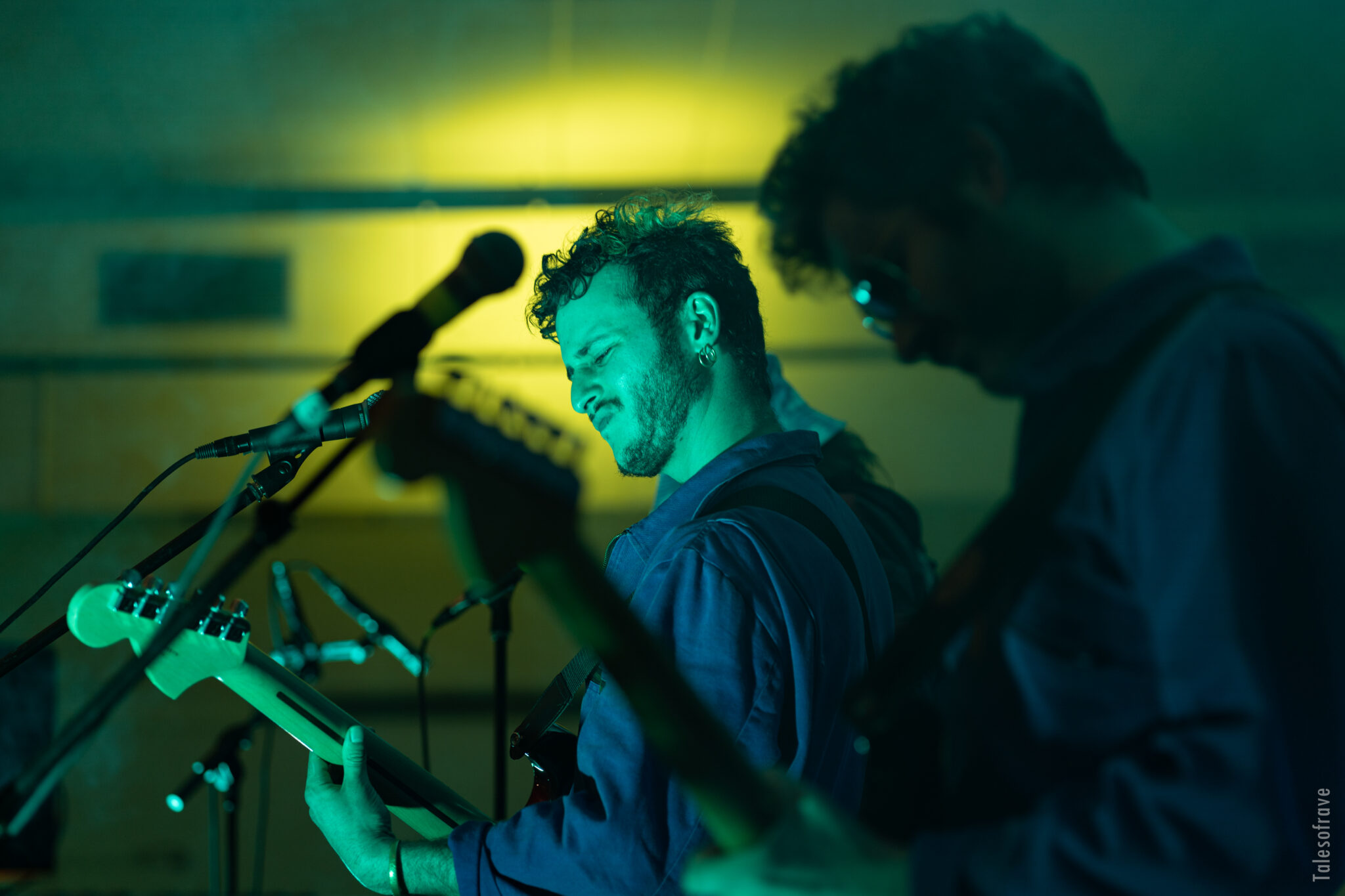 Plan de profil de deux guitaristes sur scène, visage marqué par l'émotion de la musique, lumière vert bleutée